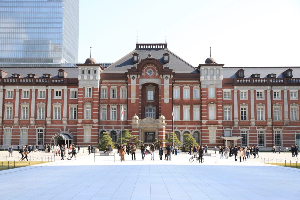 快晴の空の下に立つ、赤レンガが象徴的な東京駅丸の内駅舎と、多くの人々が行き交う駅前広場